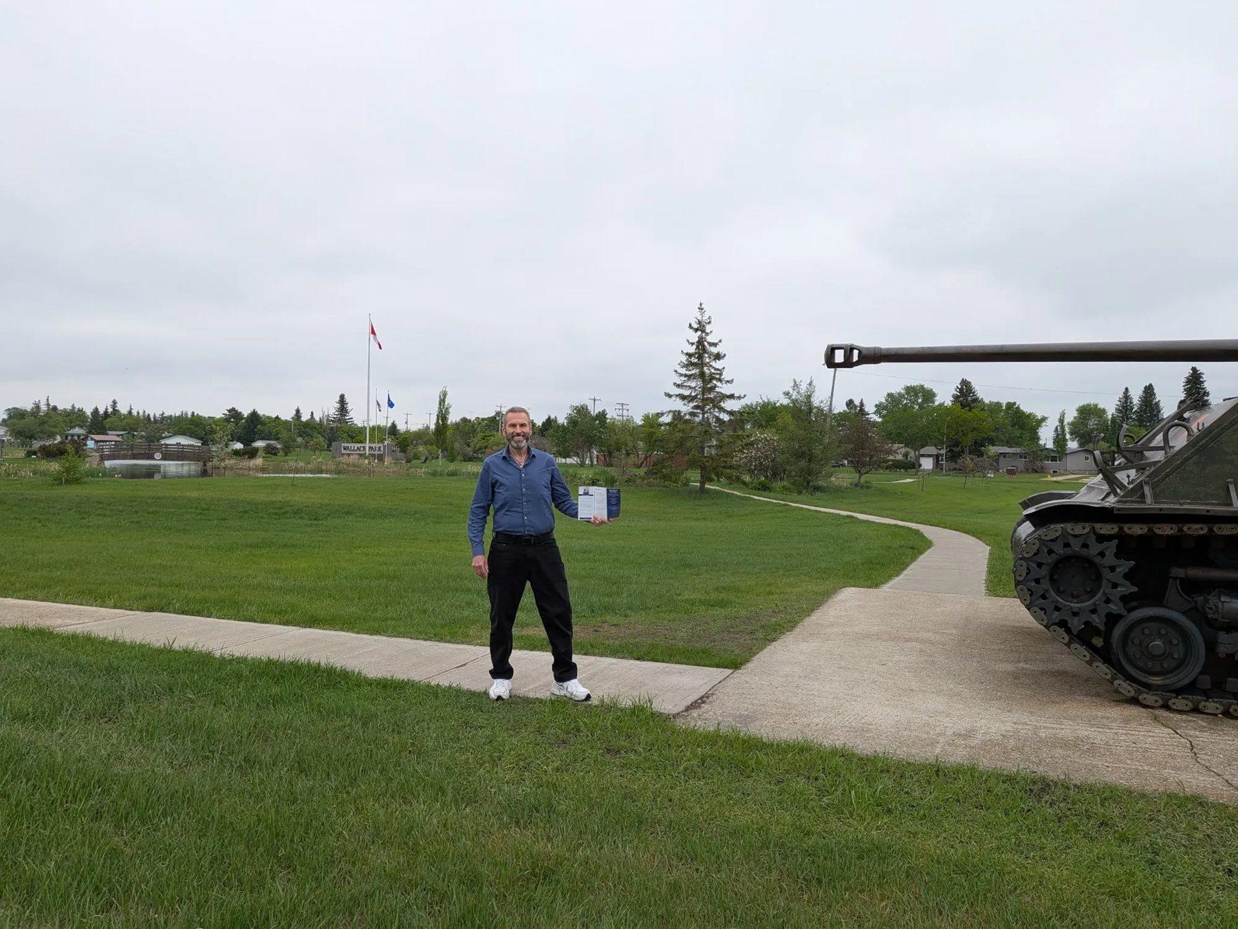 Stacy Miskew holding campaign literature beside the memorial tank in Wallace Park, Wainwright